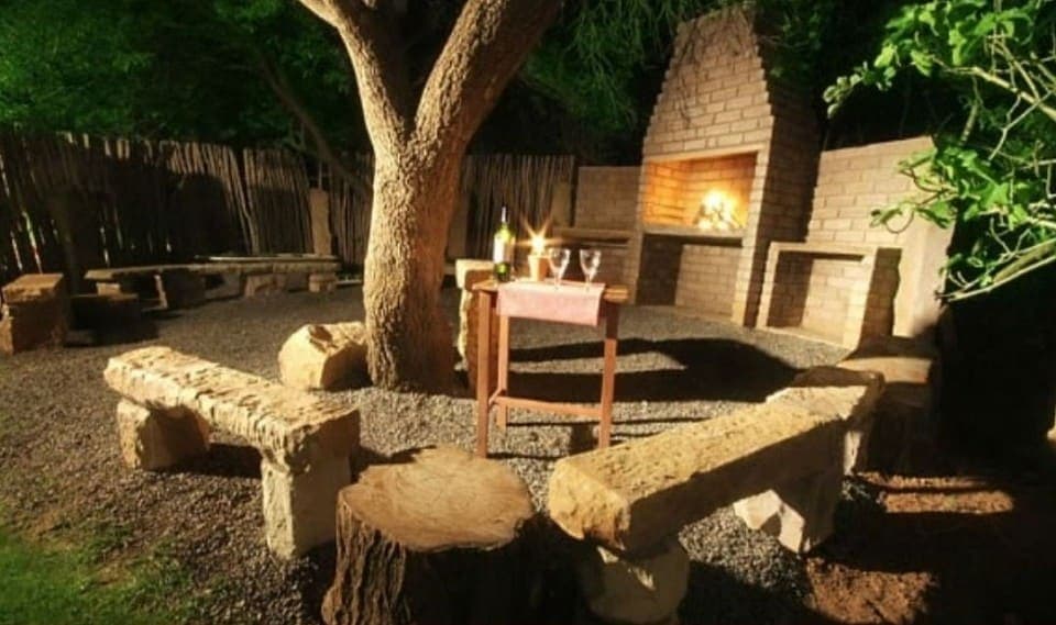 The braai area at dusk, with the fire lit and a table set beneath the tree