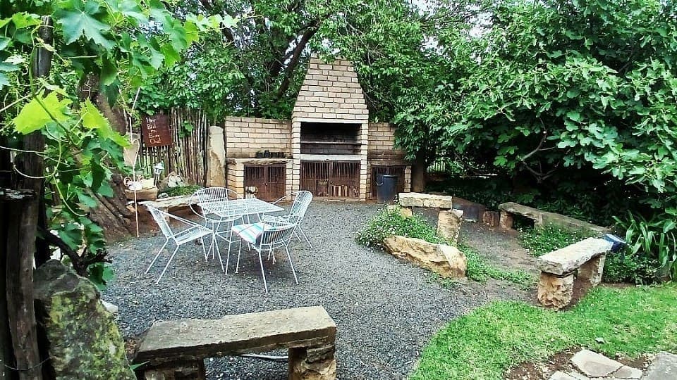 The braai area under the trees, with a brick fireplace, gravel floor and stone benches