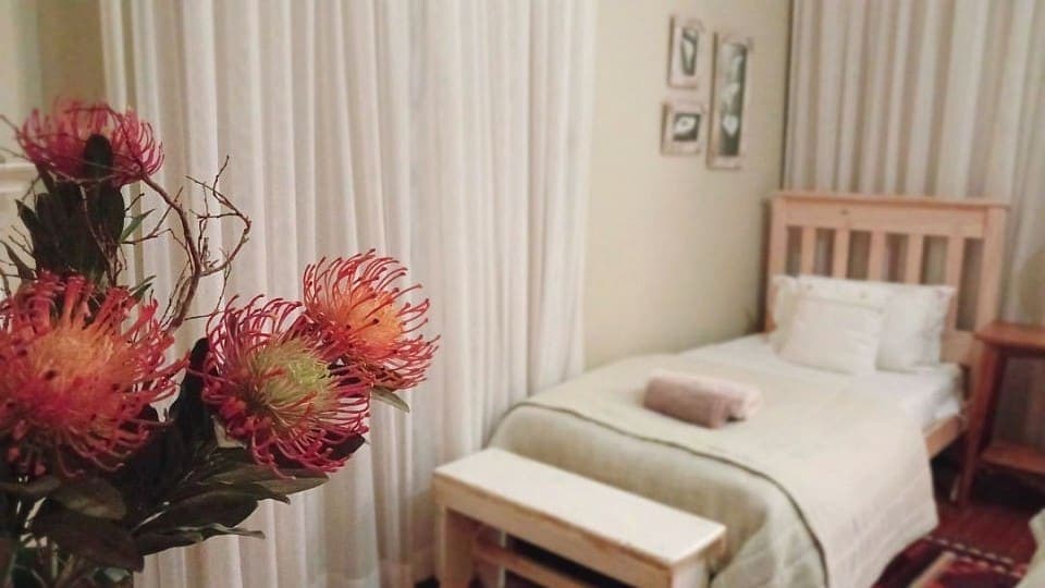 Calamus: a single bed beside a vase of proteas, with the window curtains behind