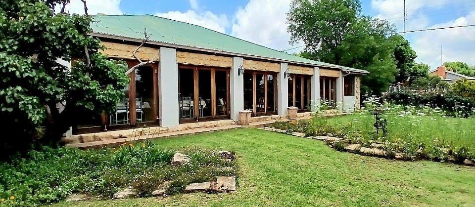 The front of House Beautiful, a low sandstone guesthouse with a green roof and a shaded stoep