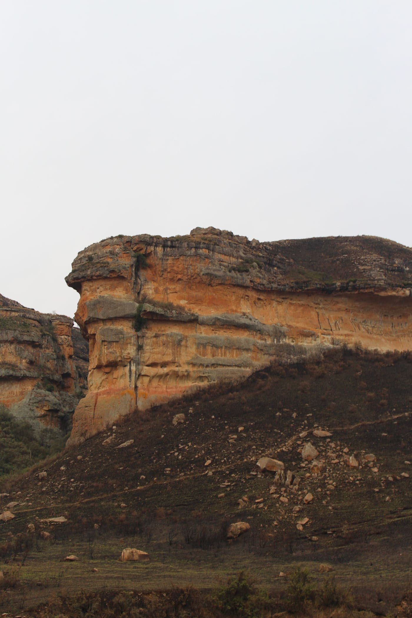 Layered ochre sandstone cliffs above a slope of burnt grass in the Golden Gate Highlands National Park