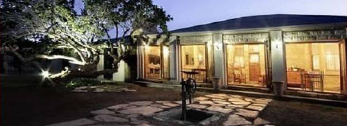 House Beautiful at night, its windows lit and the garden trees lit from below